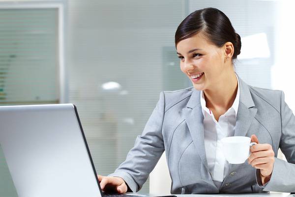 Happy woman working on a computer drinking coffee